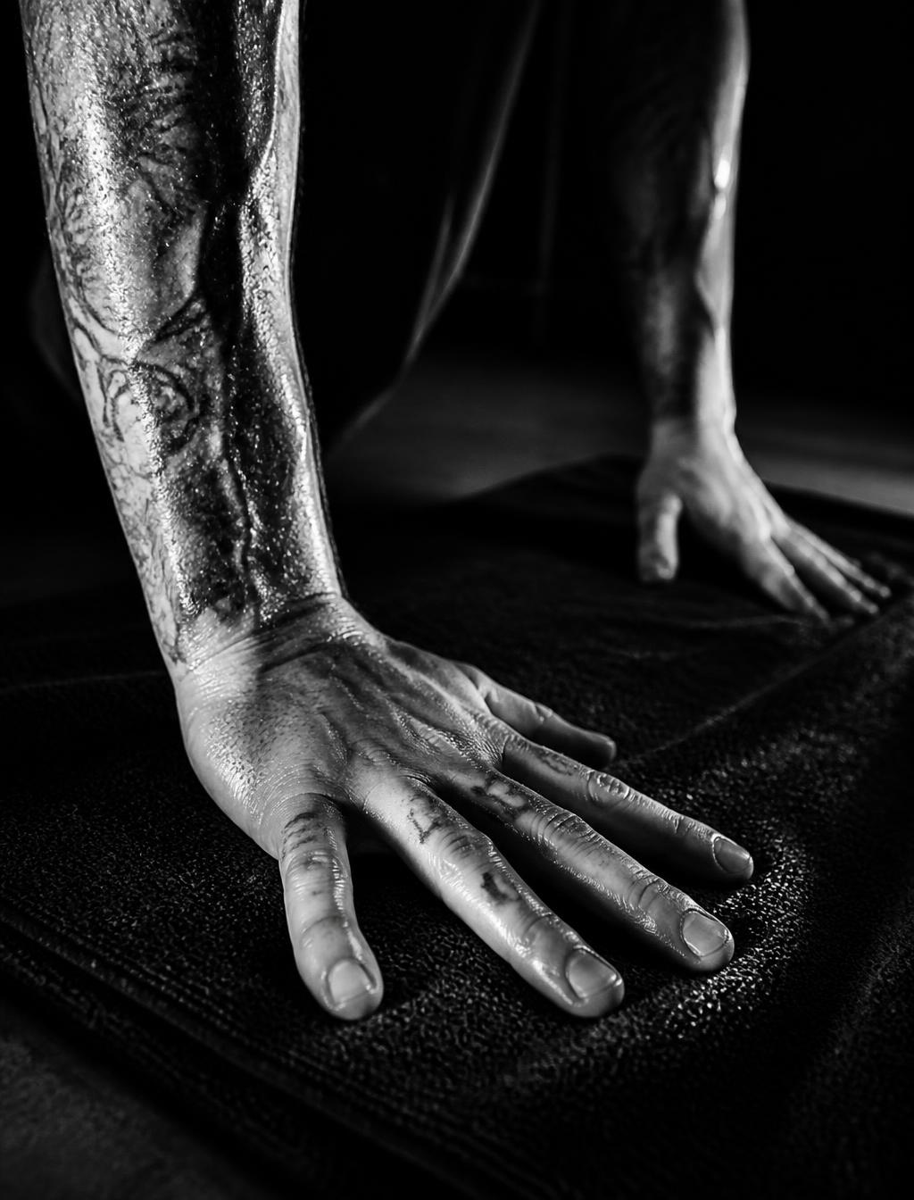 Tattooed hands pressing into a black yoga towel in darkness