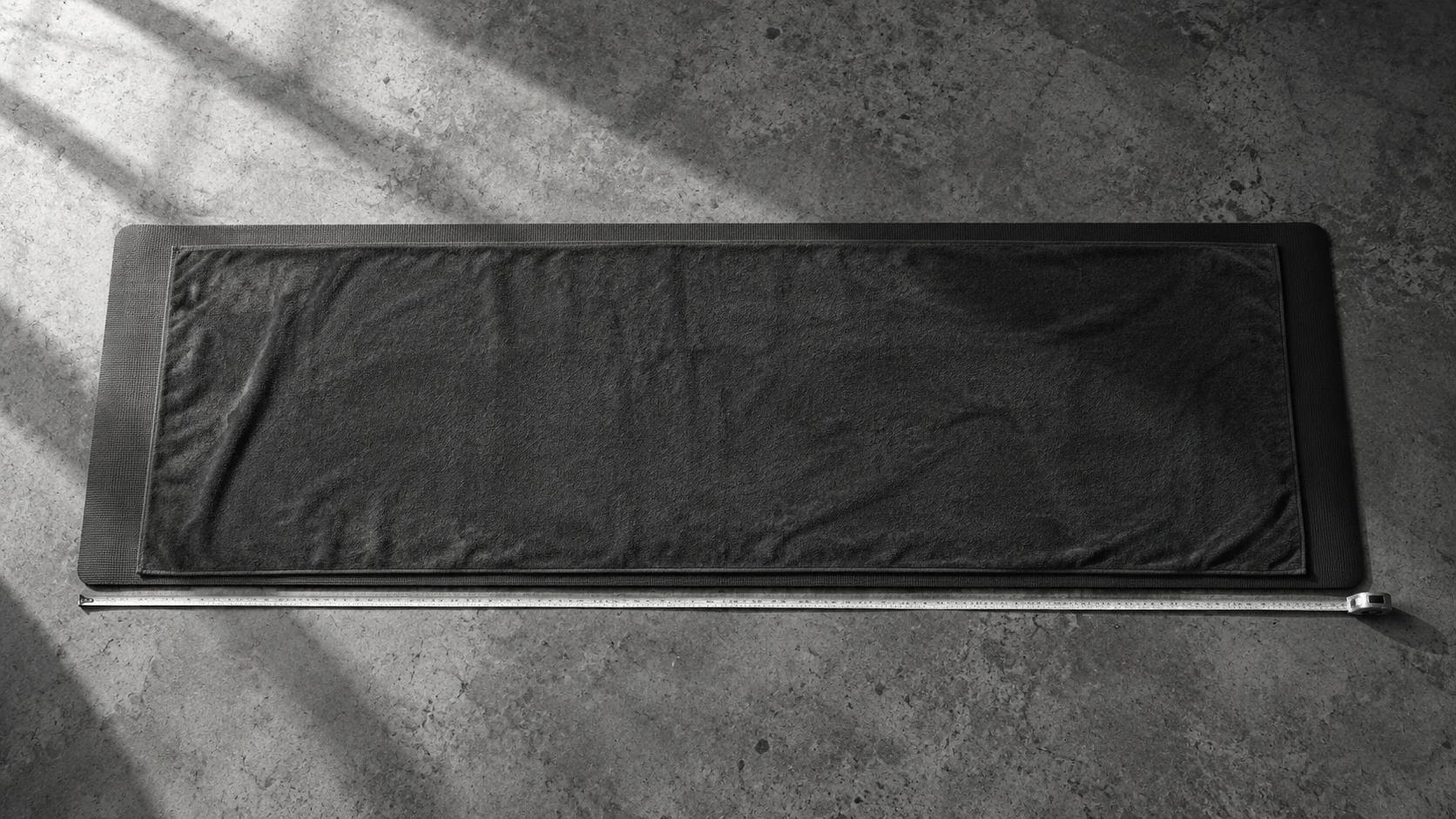 A yoga towel laid on a mat with a measuring tape alongside its length.